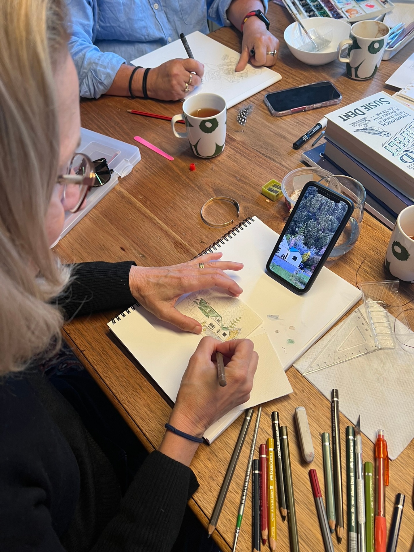 Artist sketching from a reference photo at the cottage table